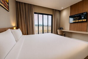 A hotel room with a large bed, a desk, a TV, and a balcony with a view.