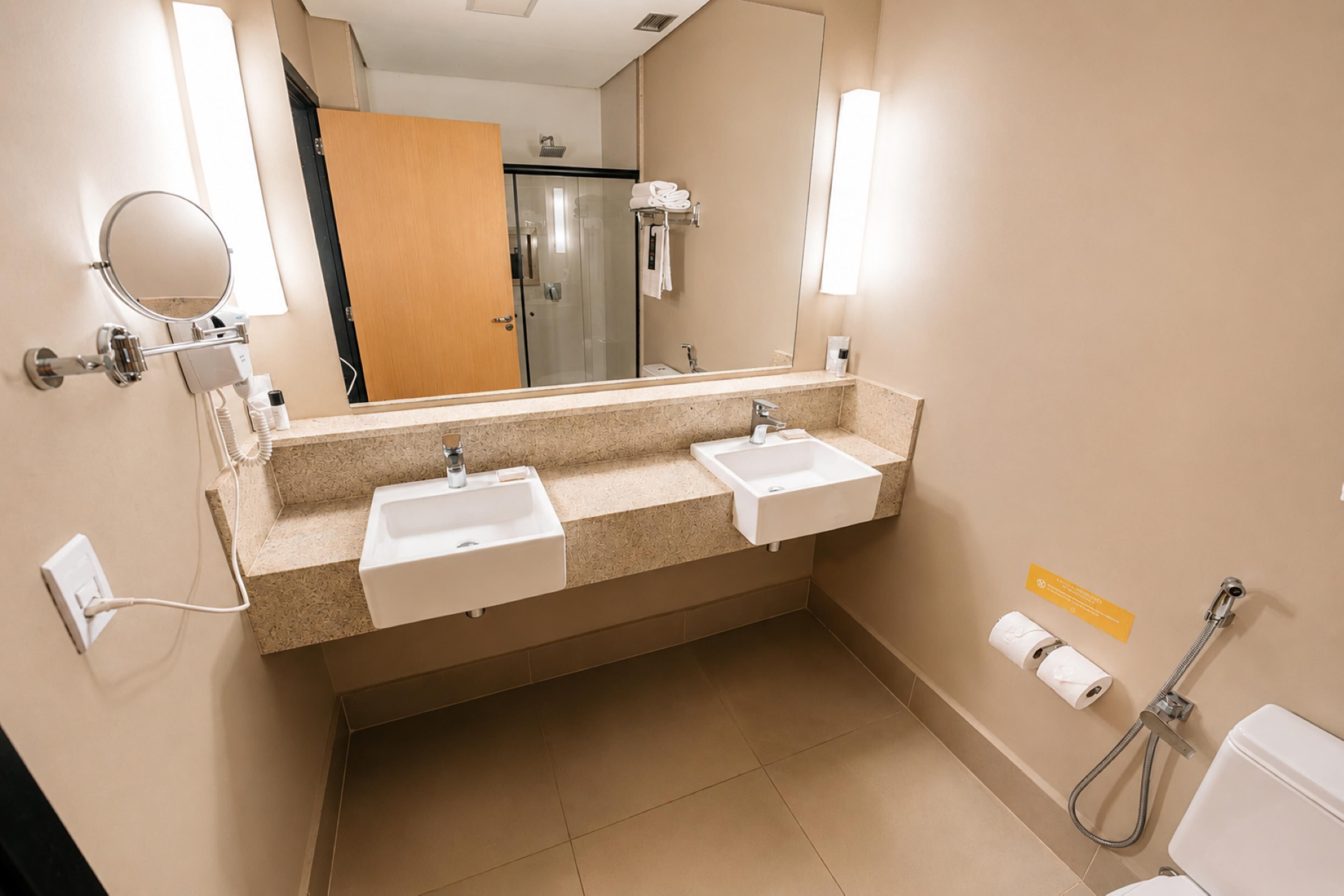 Un baño con dos lavamanos, un espejo, toallero, ducha e inodoro.