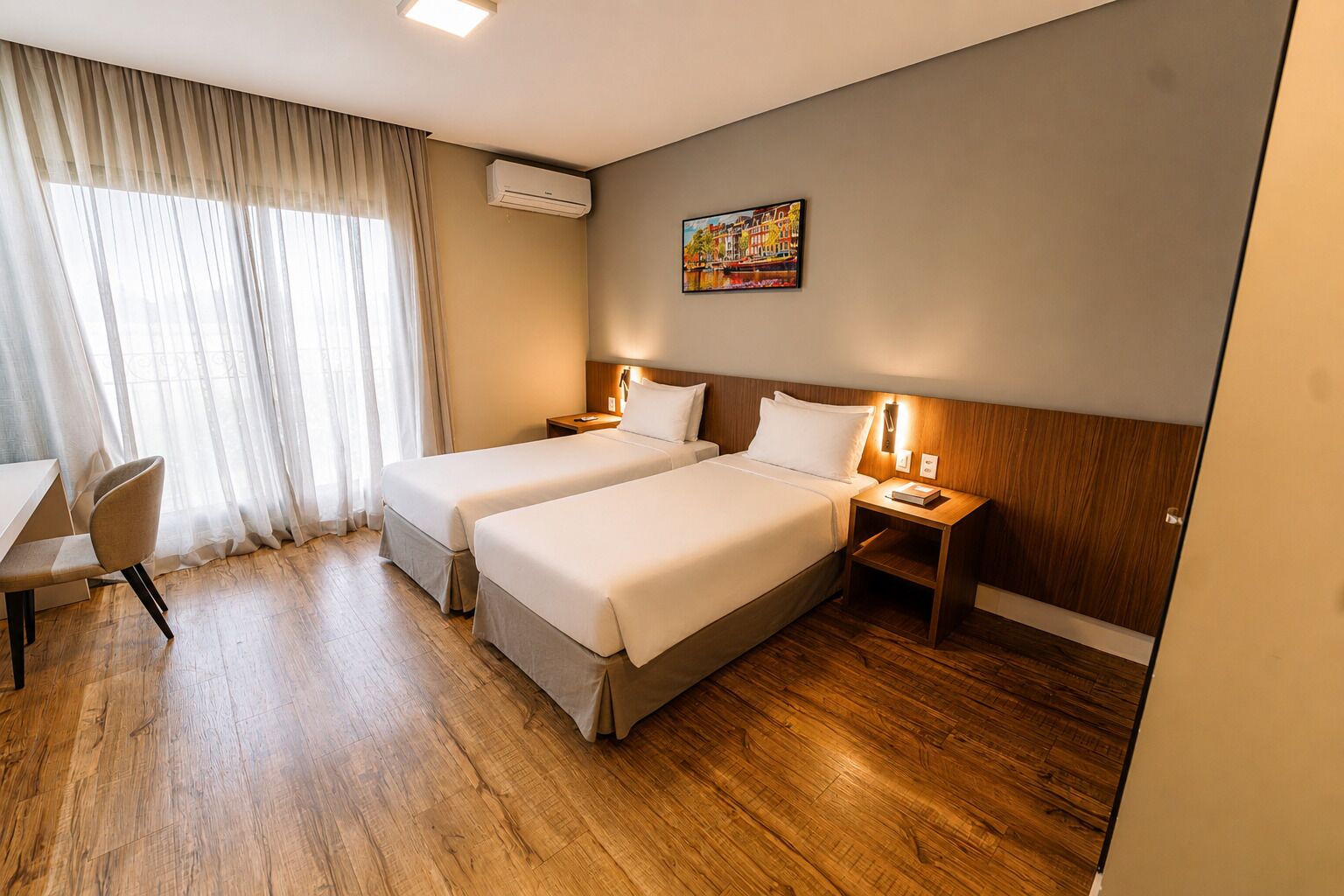 Een hotelkamer met twee bedden, een bureau, een stoel, een airconditioning en een schilderij aan de muur.