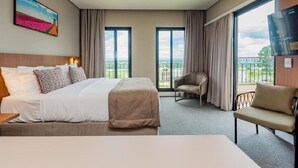 A hotel room with a bed, a chair, a sofa, a TV, and large windows.