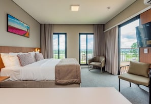 Una habitación de hotel con cama, sillón, sofá, televisión y ventanas amplias.