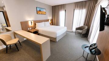 Une chambre d’hôtel avec un lit, un bureau, une chaise, une petite table, un téléviseur et un tableau au mur.