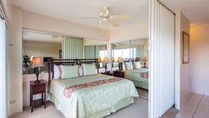 Ein geräumiges Schlafzimmer mit einem großen Bett, einem Deckenventilator und einem Spiegel, der den Raum wiedergibt.