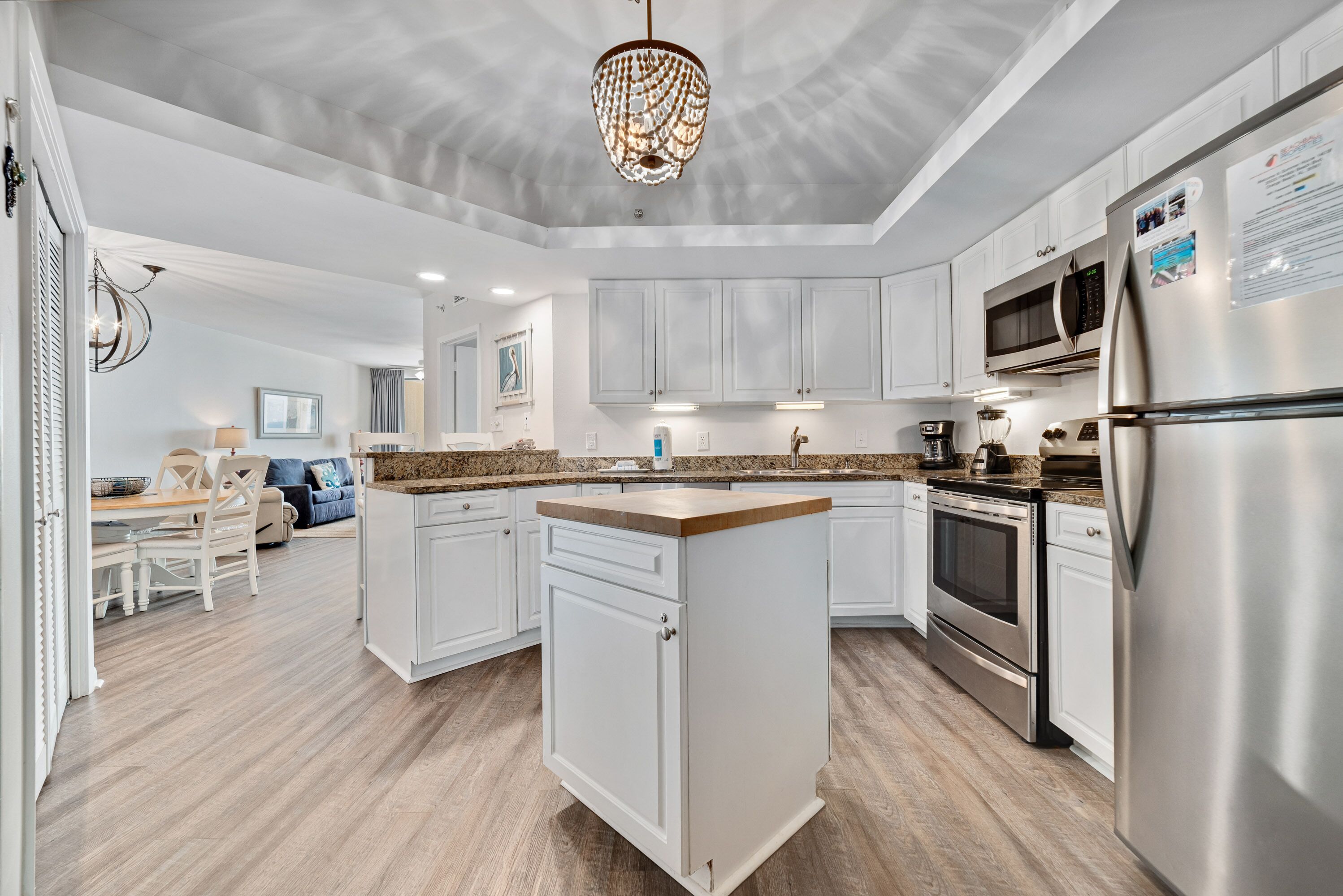 A modern kitchen with white cabinets, a central island, stainless steel appliances, and a chandelier.