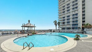 A pool area with a gazebo, lounge chairs, and a tall building in the background. - Summer House 1403B- Family friendly complex to enjoy the Beach!!! (Orange Beach)