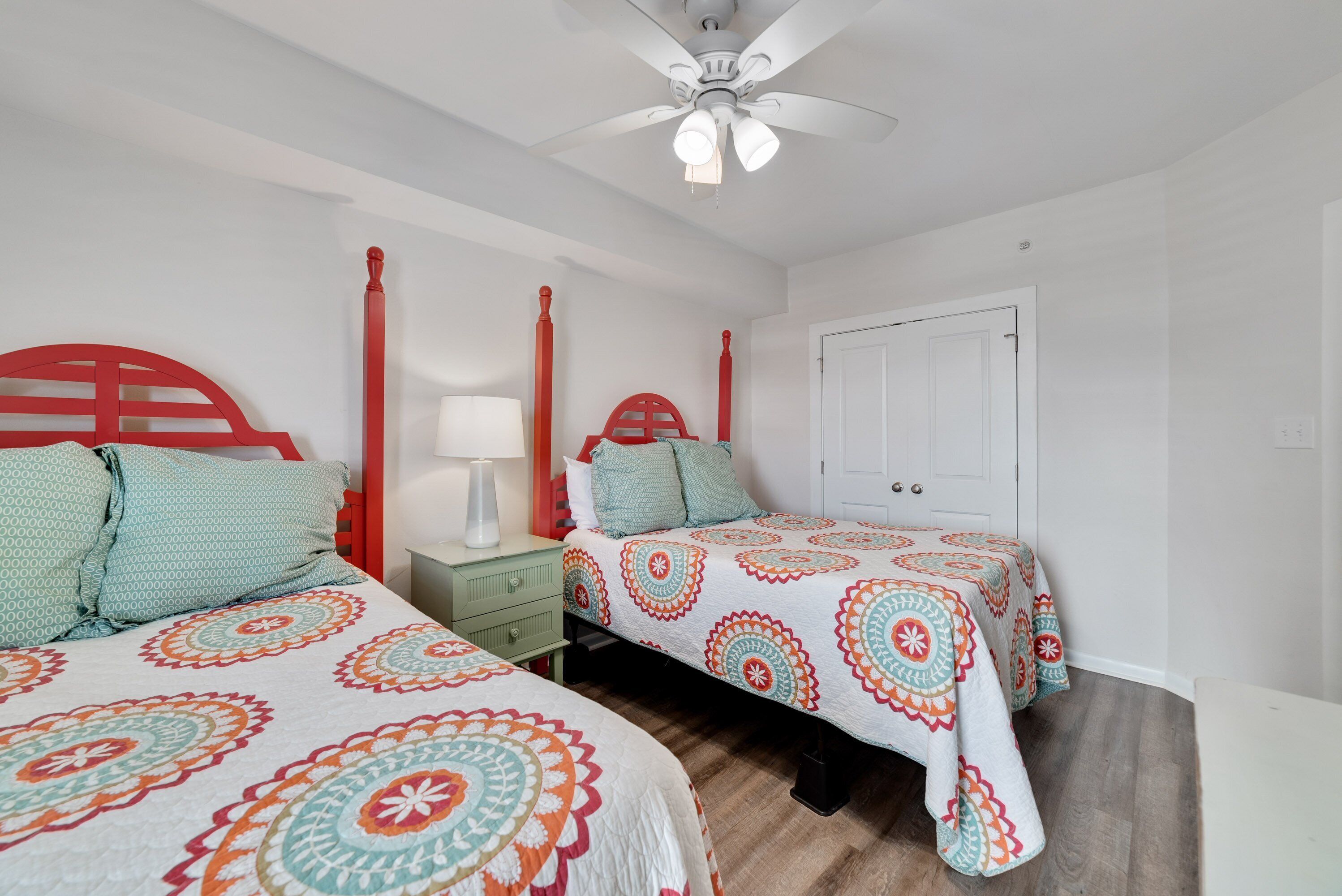 A bedroom with two beds, each with a red headboard, a white ceiling fan, and a white door.