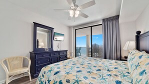 A hotel room with a bed, a dresser, a chair, a ceiling fan, a large window with curtains, and a view of the outdoors. - Summer House 1403B- Family friendly complex to enjoy the Beach!!! (Orange Beach)