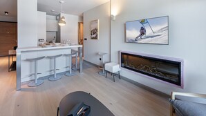 A modern kitchen with a bar area, a fireplace, and a ski-themed painting. - Wellness Getaway: Modern Apartment in Megève with Pool, Gym, and Spa Access (Megève)