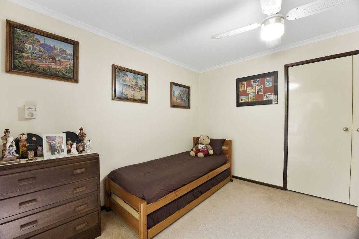 A bedroom with a single bed, a dresser, a ceiling fan, and wall-mounted pictures.