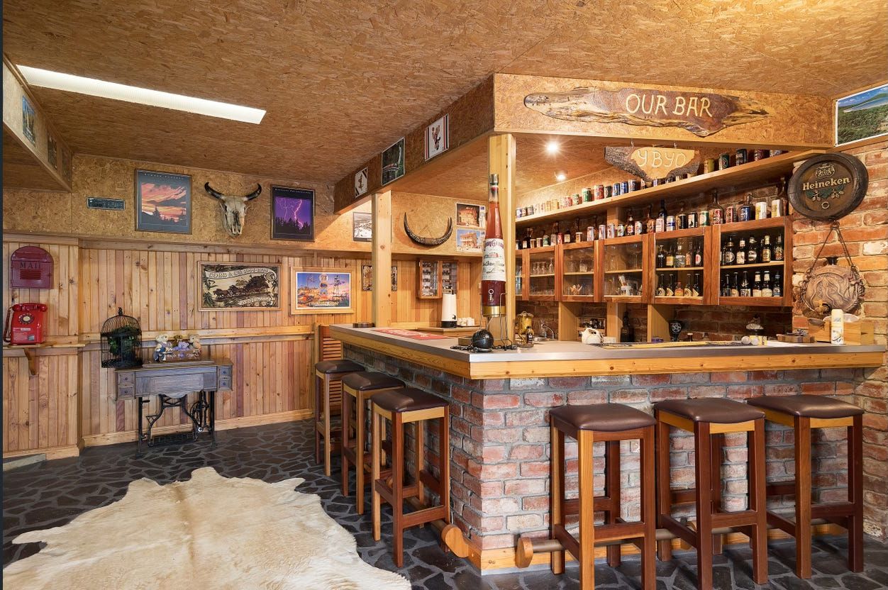 A rustic bar area with wooden shelves stocked with various bottles, a wooden counter, and bar stools.