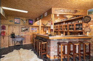 A rustic bar area with wooden shelves stocked with various bottles, a wooden counter, and bar stools. - The Perfect Getaway! (East Warburton)