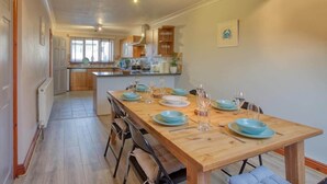 A dining area with a wooden table set for four, a kitchen in the background, and a framed picture on the wall. - Large House with Panoramic Sea Views & Parking (Newlyn)