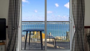 A balcony with a table and chairs, overlooking a body of water and a distant shoreline. - Large House with Panoramic Sea Views & Parking (Newlyn)