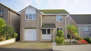 A two-story house with a garage, a front porch, and a small garden with various plants. - Large House with Panoramic Sea Views & Parking (Newlyn)