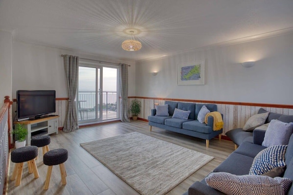 A living room with a television, sofas, a rug, and a balcony with a view.