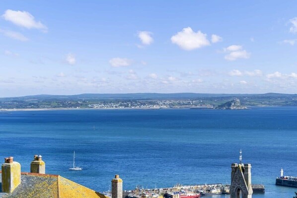 Eine Küstenstadt mit einem markanten Steinturm, einem Hafen voller Boote und freiem Blick auf das Meer und das entfernte Land.
