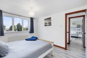 A bedroom with a bed, a window, a door, and a view of another room.