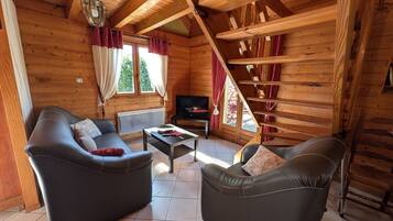 A log cabin interior with two leather sofas, a coffee table, a TV, and a staircase.
