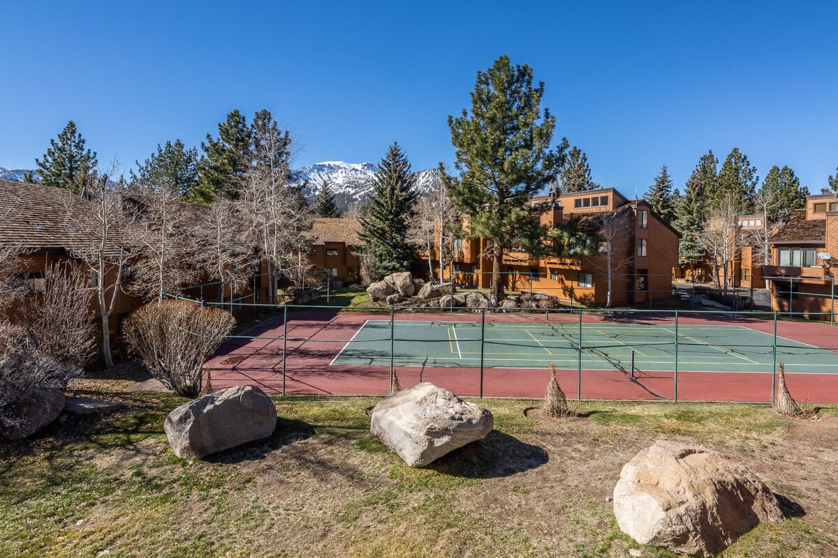 A tennis court surrounded by buildings, with a mountain in the background.