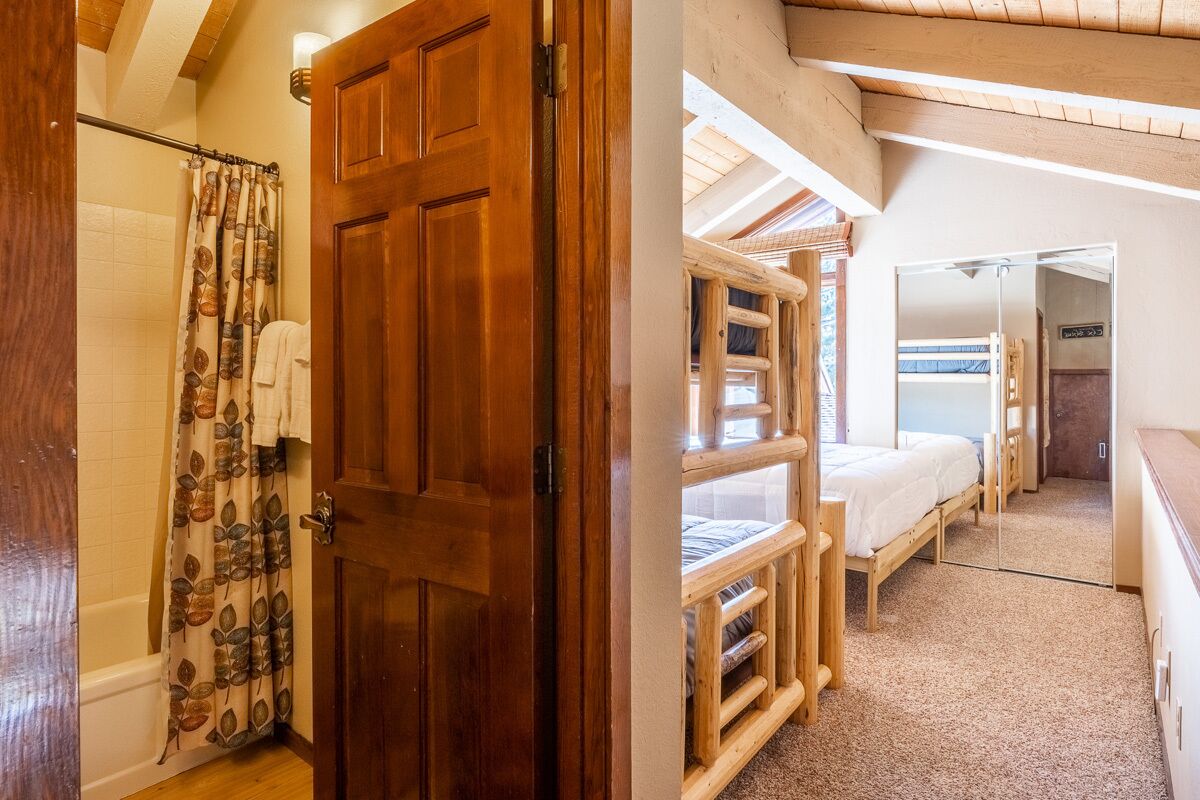 A wooden door leading to a bedroom with bunk beds and a shower area with a leaf-patterned curtain.