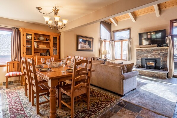 A cozy living room with a fireplace, a dining area with a wooden table and chairs, and a sofa.