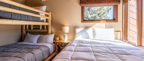 A room with two beds, a window with a view of trees, and a wooden ceiling.
