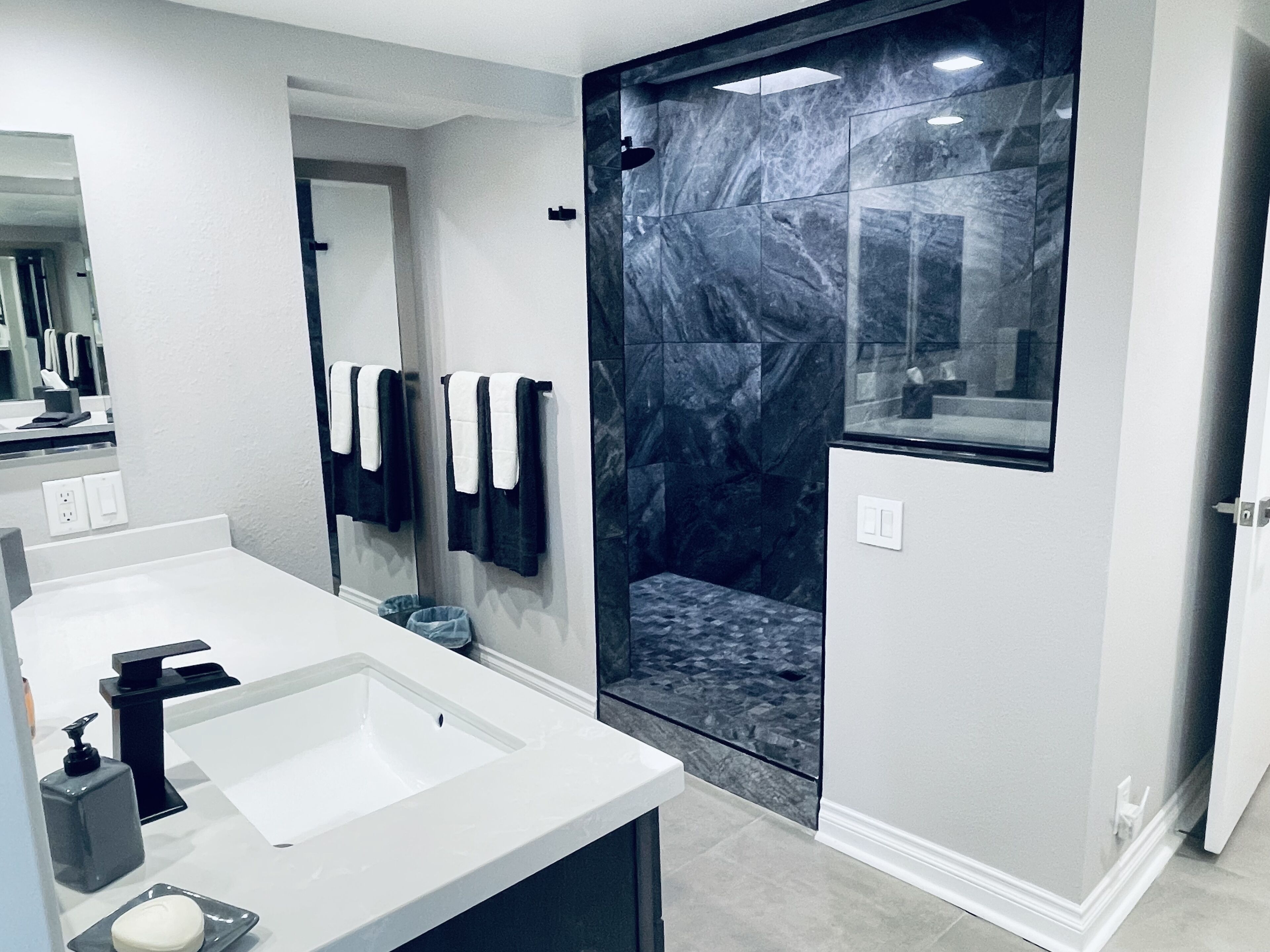 A modern bathroom with a large mirror, a white sink, and a glass-enclosed shower.