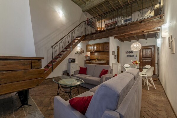 Un salon avec un escalier, un canapé, une table basse en verre et un coin repas avec des chaises.