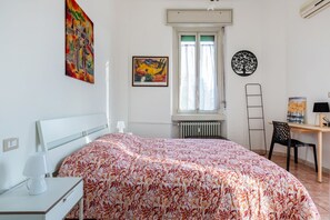 A bedroom with a bed, a desk, a chair, a radiator, and artwork on the walls.