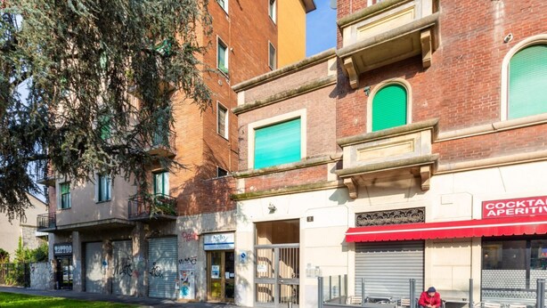 Straßenansicht mit Gebäuden, darunter eine Bar namens 'COCKTAIL APERITI' mit einer roten Markise.