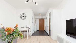 A modern living room with a TV, white furniture, a clock, and a vase of flowers.