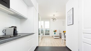 A modern kitchen with white cabinets, a coffee machine, and a dining area with a white table and chairs.