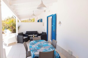 Un espace extérieur abrité, aménagé avec une table et des chaises, un canapé et une porte bleue.