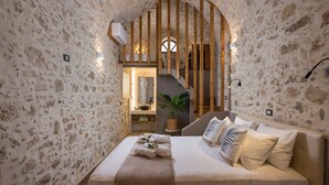 A bedroom with stone walls, a wooden staircase, a bed with white linens, and a small plant. - Casa Belvedere Boutique Villa (Apokoronas)