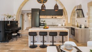 A modern kitchen with a central island, bar stools, and a piano. - Casa Belvedere Boutique Villa (Apokoronas)