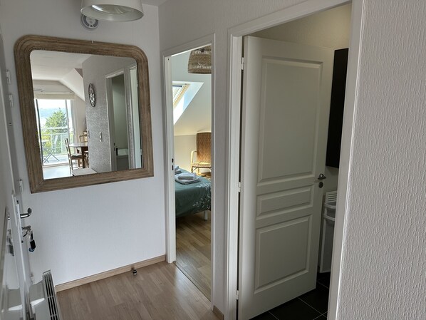 A hotel room with a large mirror, a bed with a green bedspread, a small table, and a chair. - Apartment with ocean view 🌊 facing south ☀️ in Carantec (Carantec)
