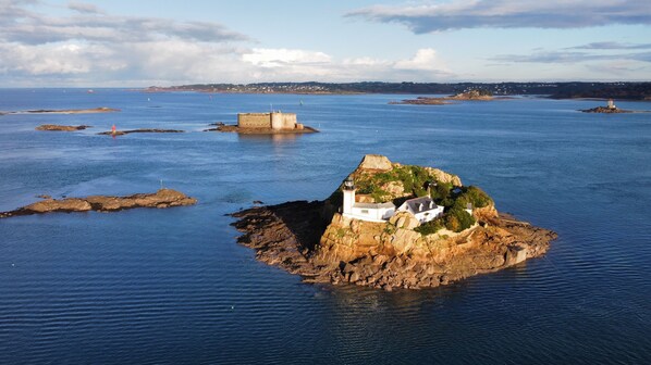 A coastal scene with a prominent white building on a rocky island, surrounded by calm blue waters.