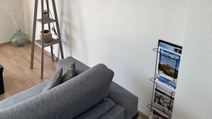 A room with a grey sofa, a lamp, a painting of a beach, and a magazine rack. - Apartment sea view 🌊 south facing ☀️à Carantec (Carantec)