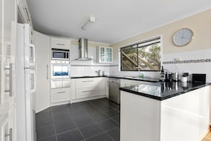 A modern kitchen with white cabinetry, a stainless steel range hood, a built-in microwave, and a dishwasher. - Marengo Panoramic Ocean Views (Marengo)