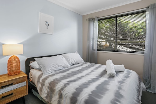 A neatly made bed with a striped bedspread, a bedside lamp, a framed picture on the wall, and a window with curtains. - Marengo Panoramic Ocean Views (Marengo)