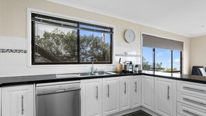 A modern kitchen with white cabinets, a dishwasher, a sink, and a window with a view of trees. - Marengo Panoramic Ocean Views (Marengo)