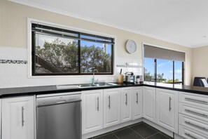 Eine moderne Küche mit weißen Schränken, einem Geschirrspüler, einer Spüle und einem Fenster mit Blick auf Bäume.