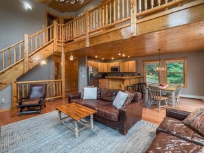 A spacious living area with a wooden staircase, a kitchen, and a dining area.