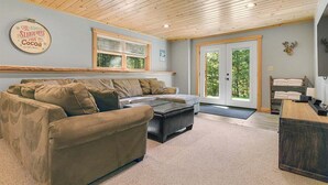 A cozy living room with a wooden ceiling, a sofa, a coffee table, and a door leading outside.