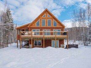 A wooden cabin with a balcony, large windows, and a snow-covered landscape.