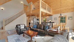 A spacious living area with a high ceiling, a staircase leading to an upper level, a kitchen, and a dining area.