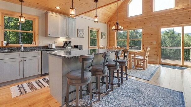 A spacious kitchen with a central island, bar stools, and large windows offering views of the outdoors.