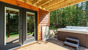 A wooden deck with a hot tub, a wooden pergola, and a glass door leading to a deck.
