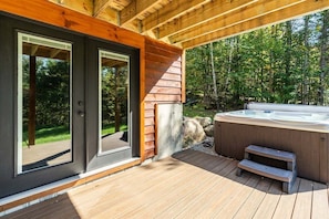 A wooden deck with a hot tub, a wooden pergola, and a glass door leading to a deck.