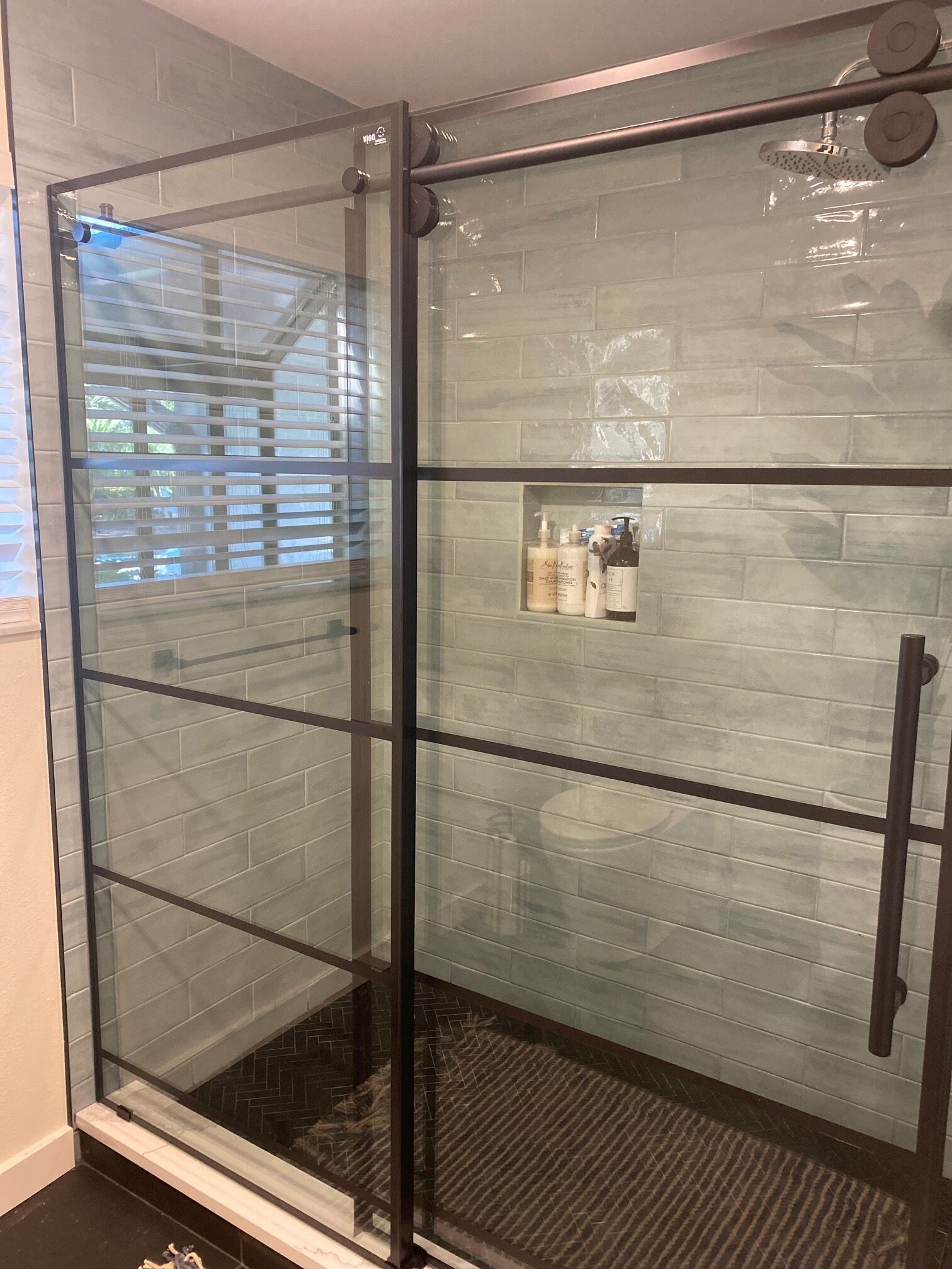 Une douche fermée par des parois de verre, avec un mur carrelé et une petite étagère contenant des articles de toilette.